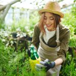 A woman in an overalls and hat holding a bottle of water.